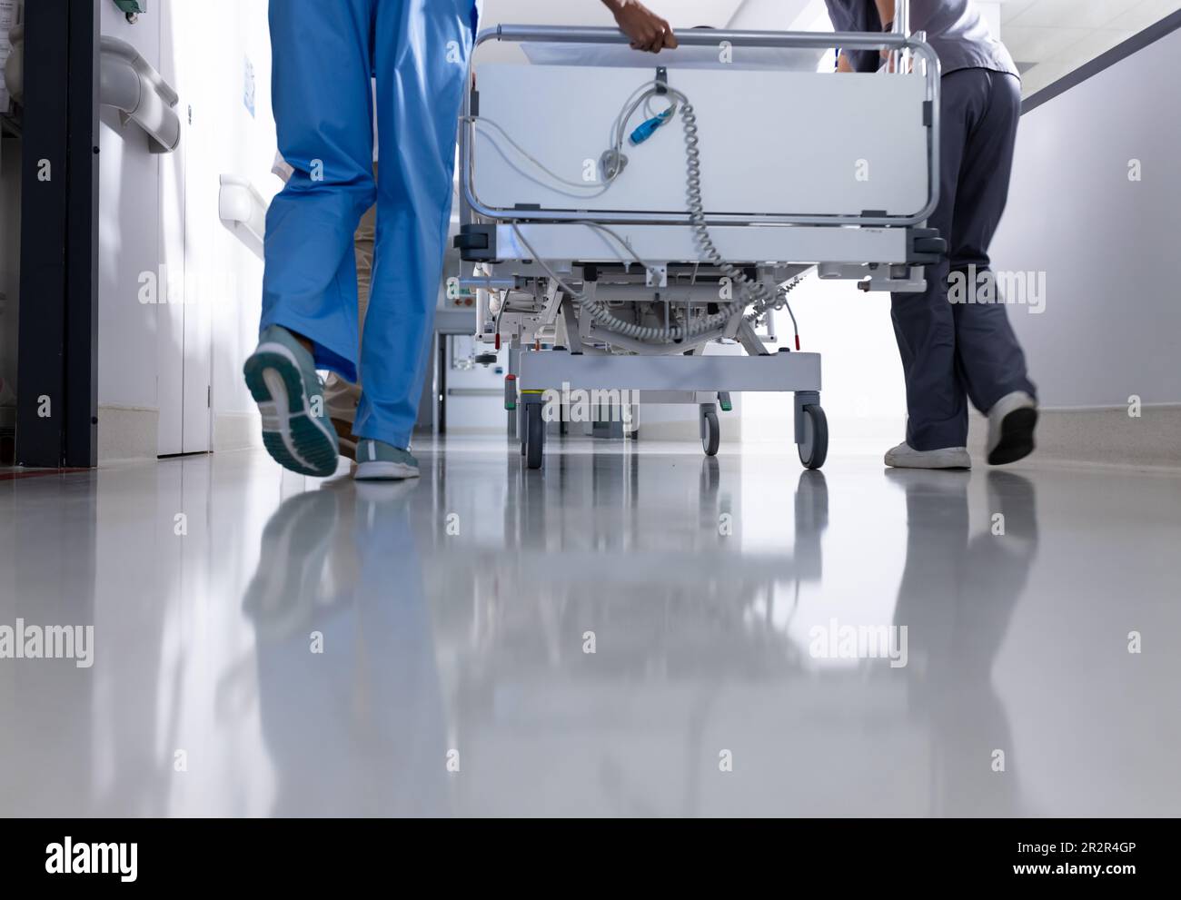 Unterer Teil von verschiedenen Ärzten, die Patienten im Krankenhausbett den Flur hinunterschieben Stockfoto