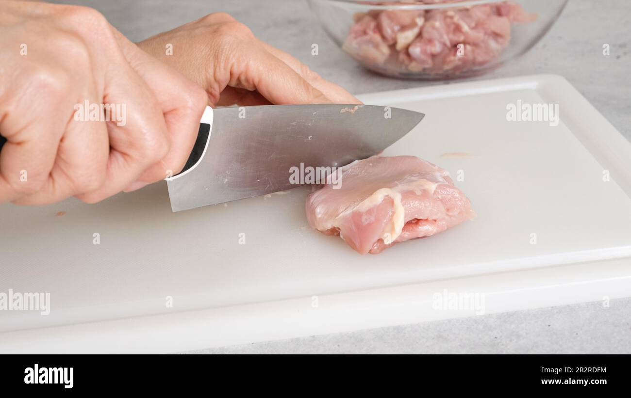 Der Koch schneidet rohes Hähnchenfleisch auf einem weißen Schneidebrett aus Kunststoff, Nahaufnahme, Zubereitungsprozess, Rezept Stockfoto