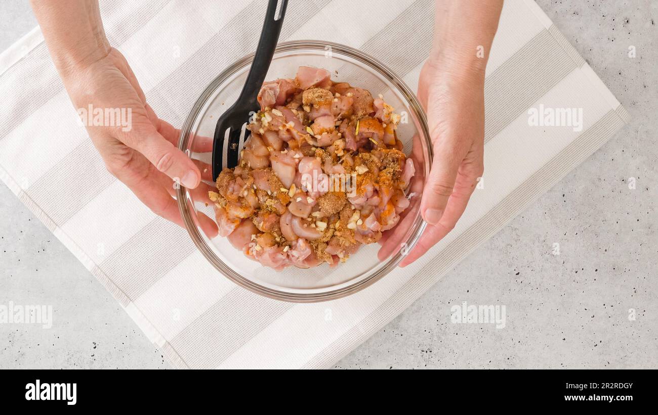 Glasschüssel mit der gehackten marinierten Hähnchenfleischmischung innen, flach liegend, Kopierraum, Frauenhände Stockfoto