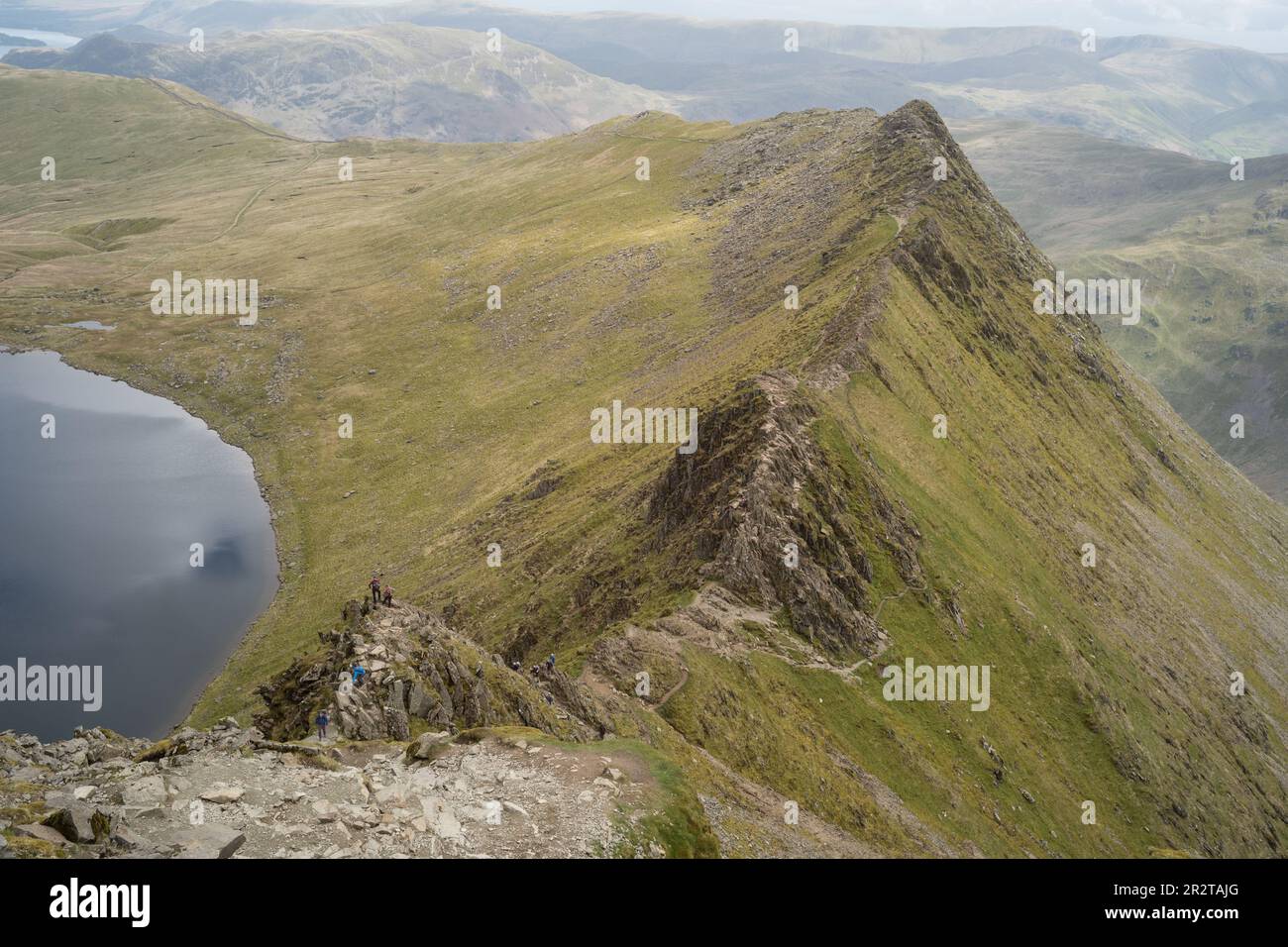 Wanderer auf dem Weg am Rand mit Helvellyn-Gipfel dahinter Stockfoto