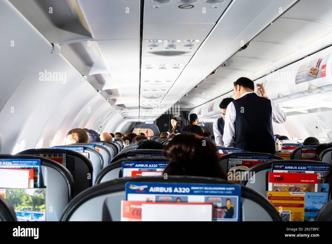 Männliche Flugbegleiter servieren Passagieren Mahlzeiten und Getränke in einer Flugkabine Boeing 737, die von türkischen Pegasus Airlines betrieben wird Stockfoto