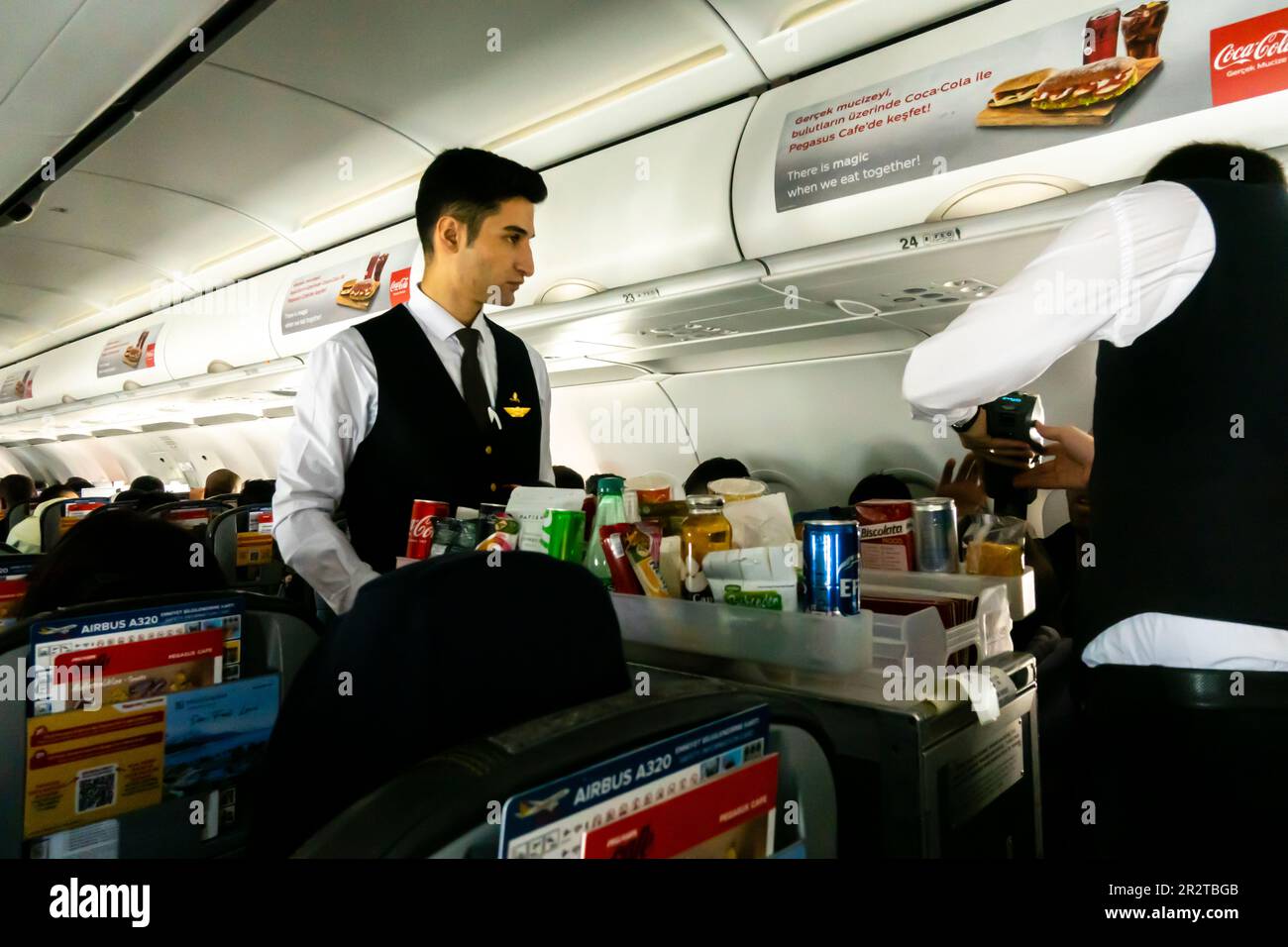 Männliche Flugbegleiter servieren Passagieren Mahlzeiten und Getränke in einer Flugkabine Boeing 737, die von türkischen Pegasus Airlines betrieben wird Stockfoto