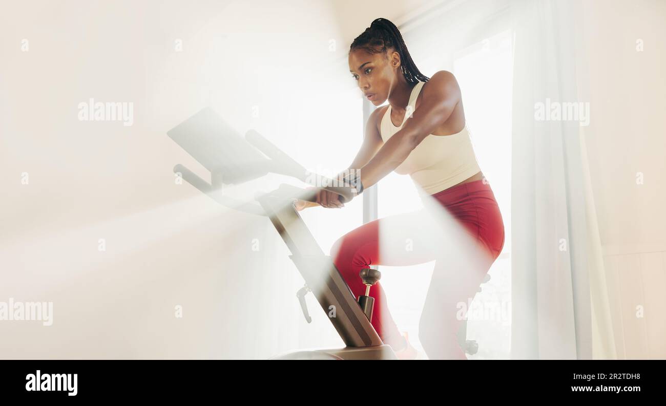 Fokussierte junge Frau, die ihr Fitnesstraining direkt anpackt und ein digitales Fahrrad als Teil ihres Heimtrainings verwendet, um motiviert und engagiert zu bleiben Stockfoto