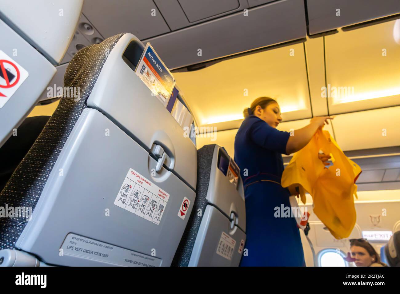 Eine Flugbegleiterin, die unscharf ist und Passagieren in einem Airbus A320-Flugzeug, das von Fly Arna betrieben wird, eine Rettungsweste vorführt Stockfoto