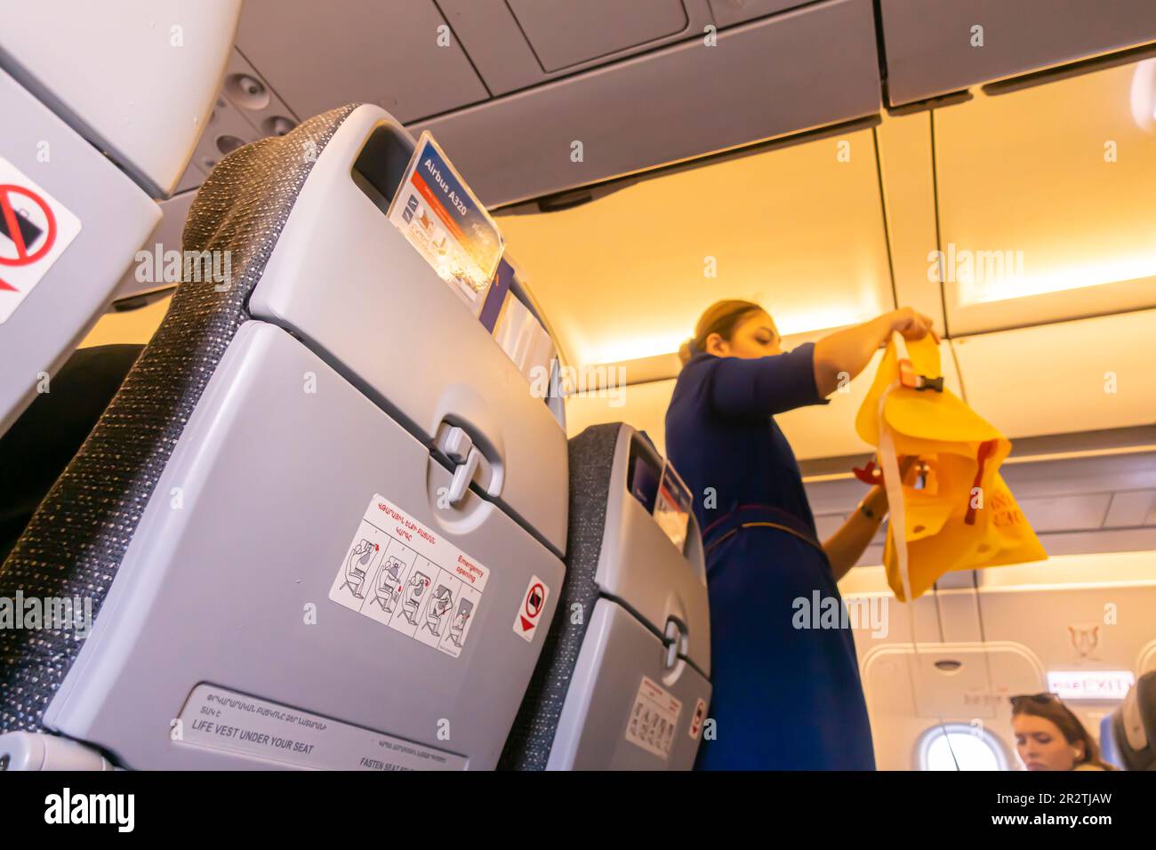 Eine Flugbegleiterin, die unscharf ist und Passagieren in einem Airbus A320-Flugzeug, das von Fly Arna betrieben wird, eine Rettungsweste vorführt Stockfoto