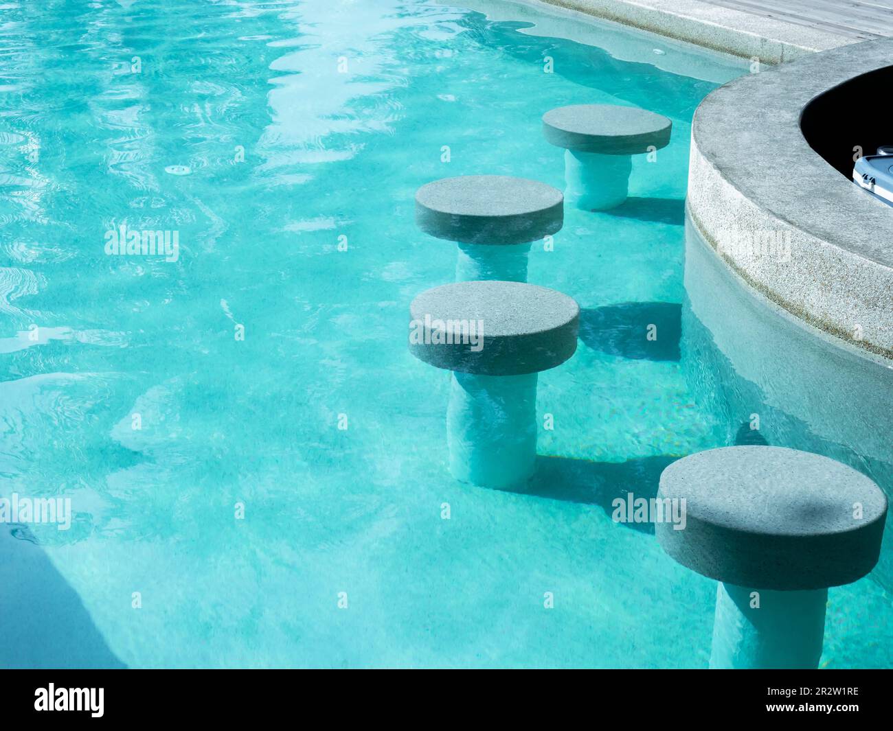 Leere runde Terrazzo Barhocker sitzen im sauberen und klaren Wasser Swimmingpool und bereiten sich auf die Gäste im Resort an sonnigen Tagen vor. Poolbar im Freien Stockfoto