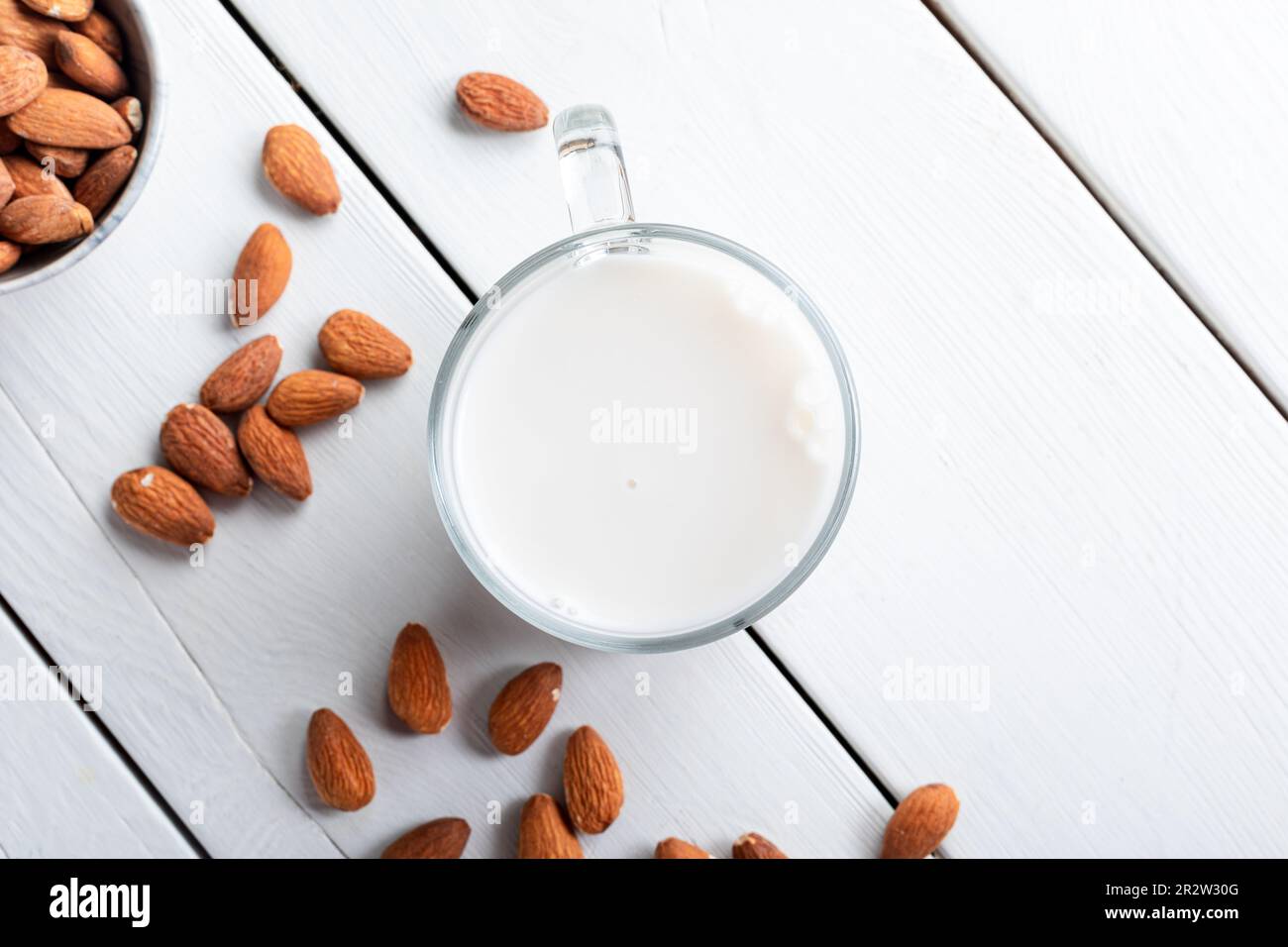 Glas Mandelmilch und Nüsse auf weißem Hintergrund, Draufsicht. Mandelmilch in Glas und Mandelnüsse auf Holzhintergrund. Stockfoto