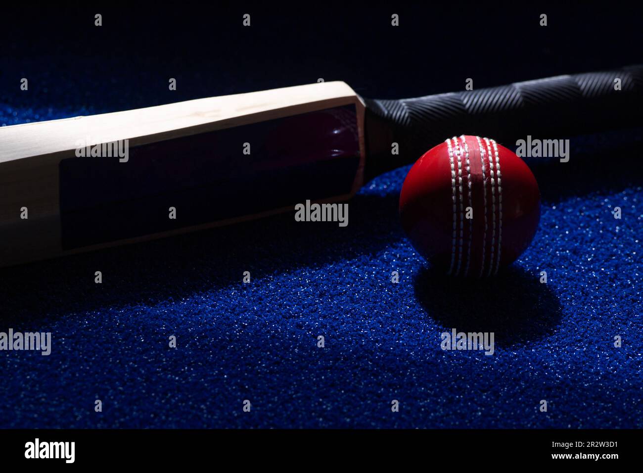 Cricketschläger und roter Ball auf blauem Hintergrund. Horizontales Sportposter, Grußkarten, Kopfzeilen, Website und App Stockfoto