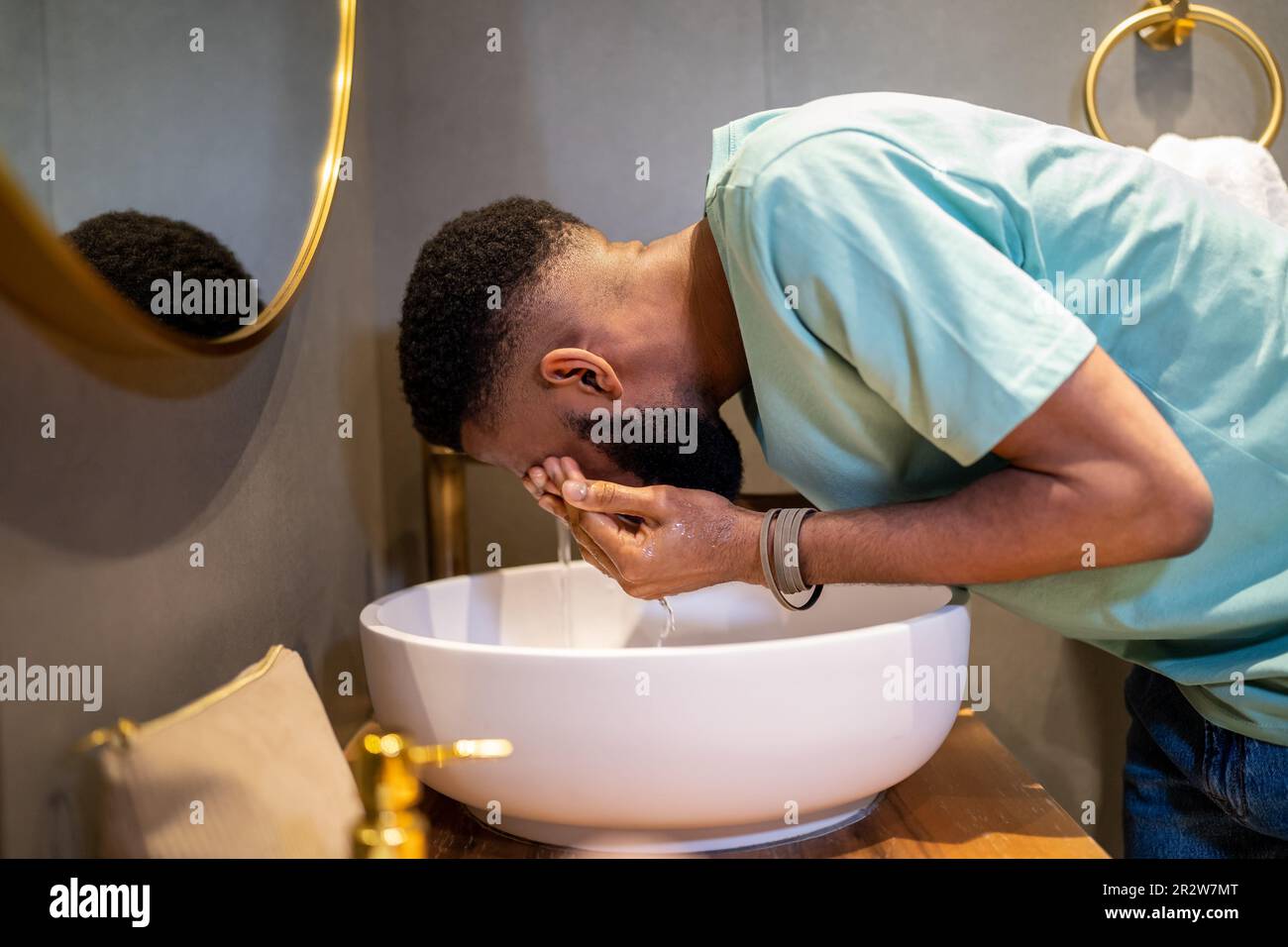 Ein müder, schläfriger afroamerikanischer Typ, der morgens sein Gesicht mit Wasser wäscht Stockfoto