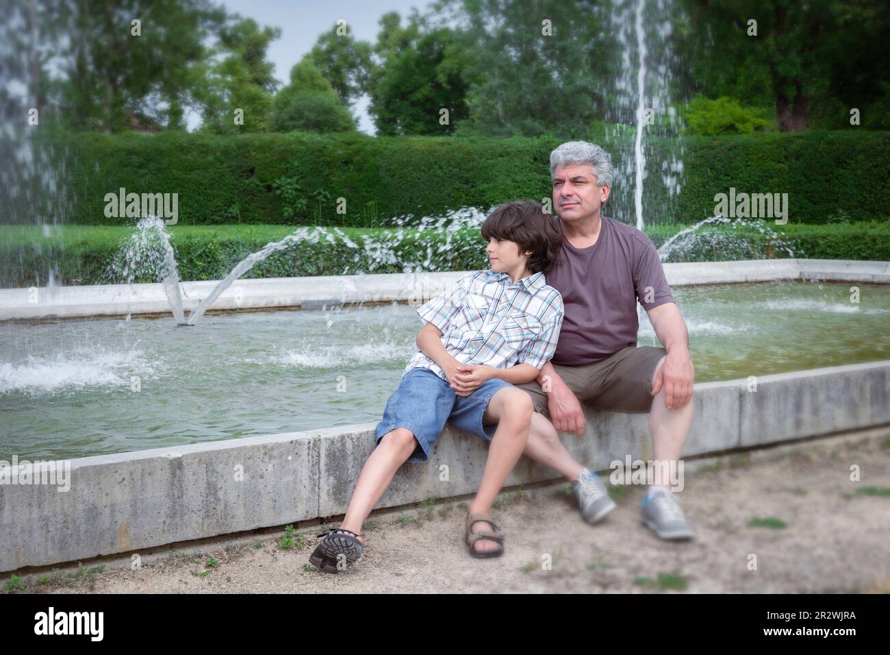 Dad und Sohn entspannen sich im Stadtpark in der Nähe der Brunnen. Viel Spaß mit der Familie. Ein glücklicher Vatertag. Stockfoto