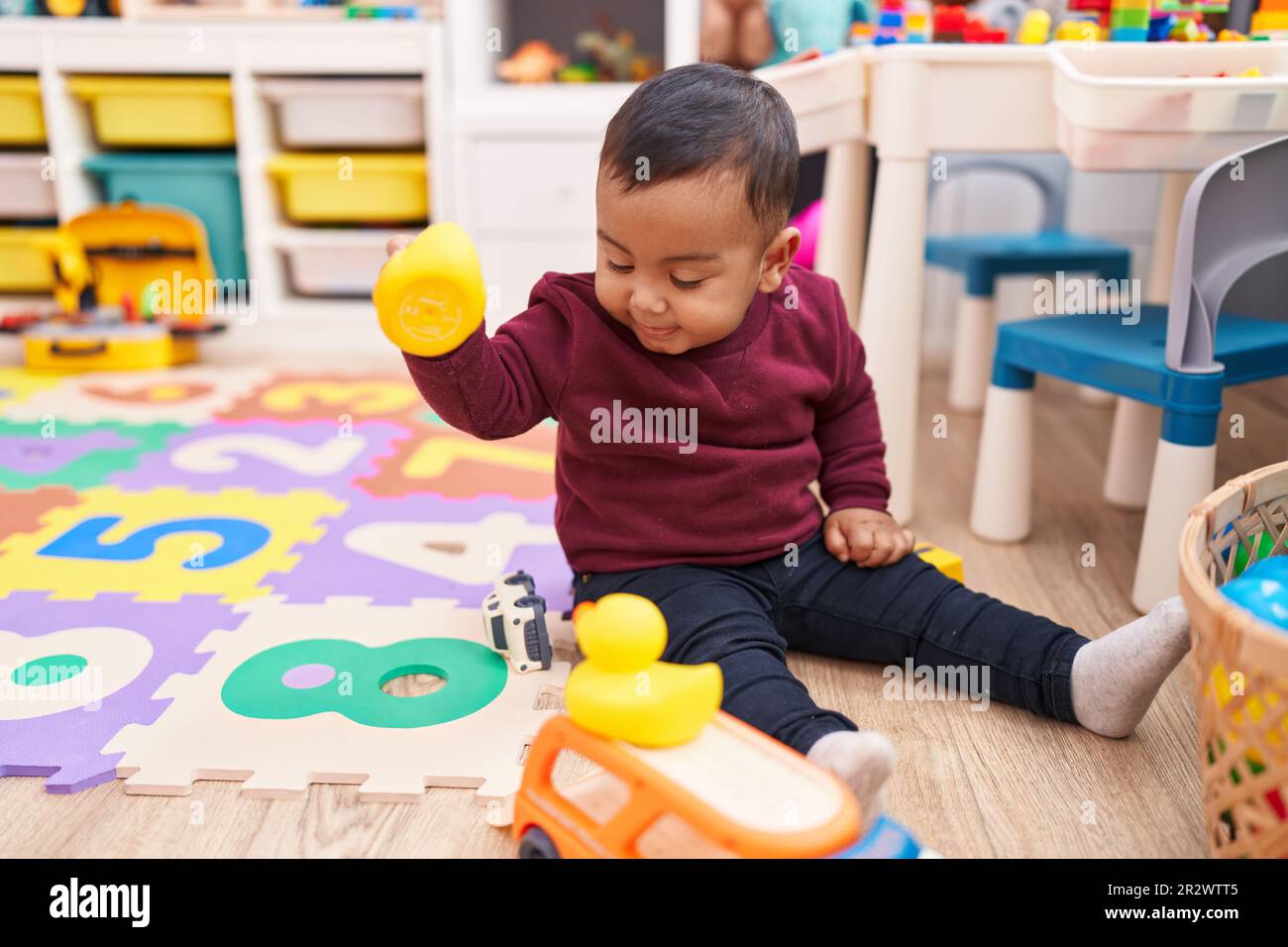Ein bezaubernder spanischer Junge, der mit Entenspielzeug spielt und im Kindergarten auf dem Boden sitzt Stockfoto