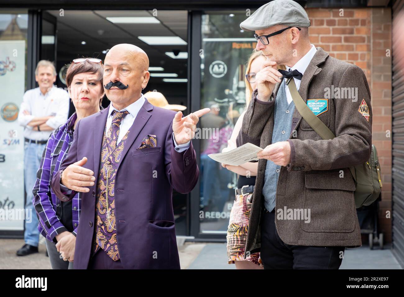 21 Mai 2023 - Warrington, Cheshire, England, Großbritannien - die Distinguished Gentleman's Ride (DGR) vereint klassische und klassische Motorradfahrer aus der ganzen Welt, um Geld und Bewusstsein für die Prostatakrebsforschung und die psychische Gesundheit von Männern zu sammeln. Eine Gruppe von Motorradfahrern aus ganz Warrington, gekleidet in ihren besten Anzügen und Krawatten, trafen sich bei ihrem Motorradhändler vor Ort und fuhren dann durch das Stadtzentrum, bevor es aus der Stadt und durch eine Kombination aus Dörfern und Städten ging. Sie erhielten vor der Fahrt Anweisungen und landeten im Besucherzentrum der Jodrell Bank. Stockfoto
