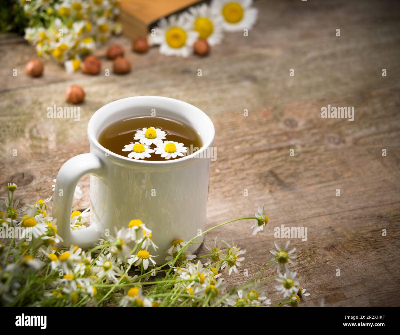 Eine Tasse Kamillentee. Bild eines Buches mit Kamille und Nüssen auf einem Holztisch. Kräutertee-Konzept für die Entspannungszeit Stockfoto