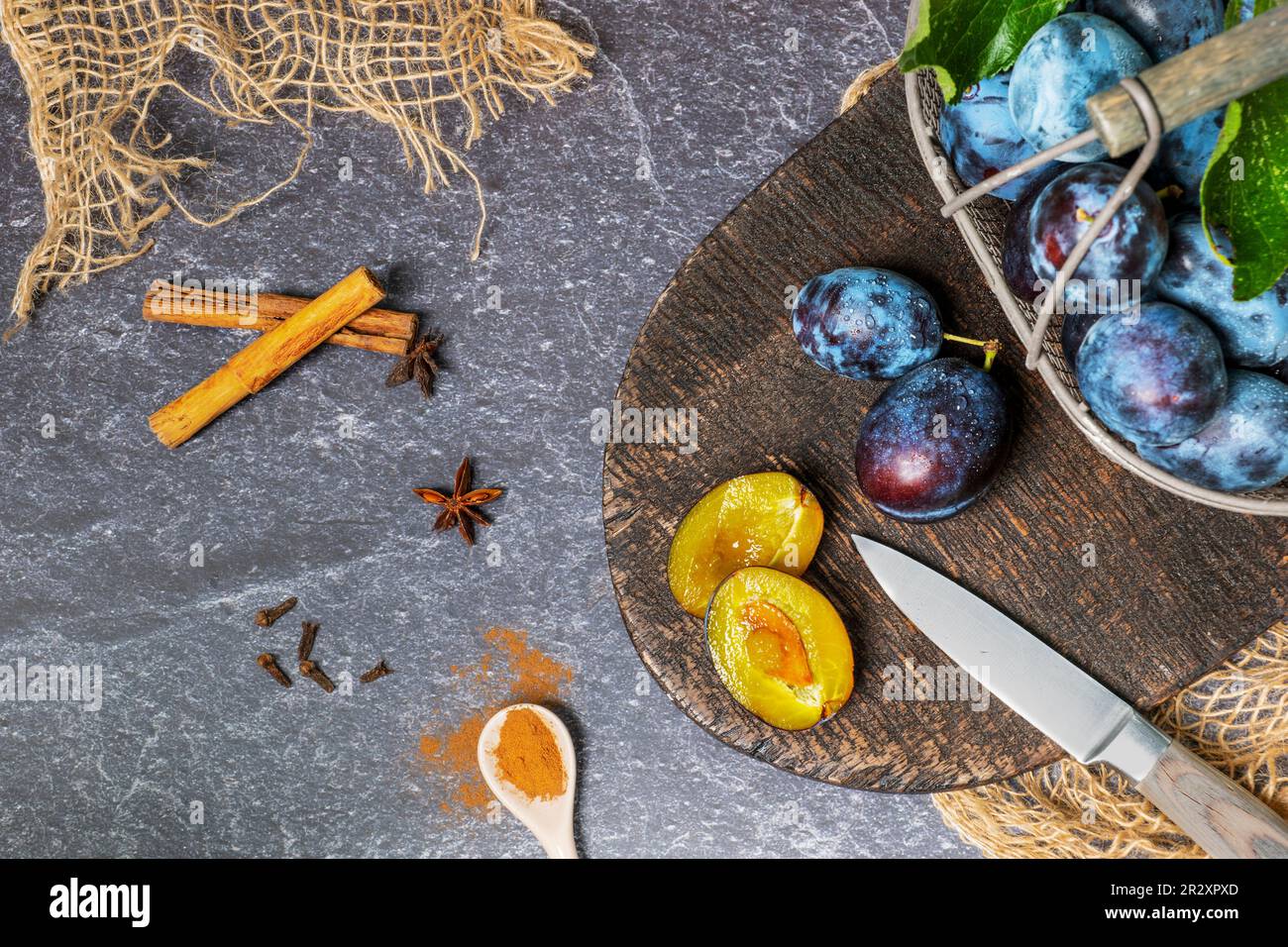 Ein Korb frisch geernteter Pflaumen wird verarbeitet. Mit typischen Gewürzen wie Zimtstäbchen, Sternanis und Gewürznelken. Stockfoto