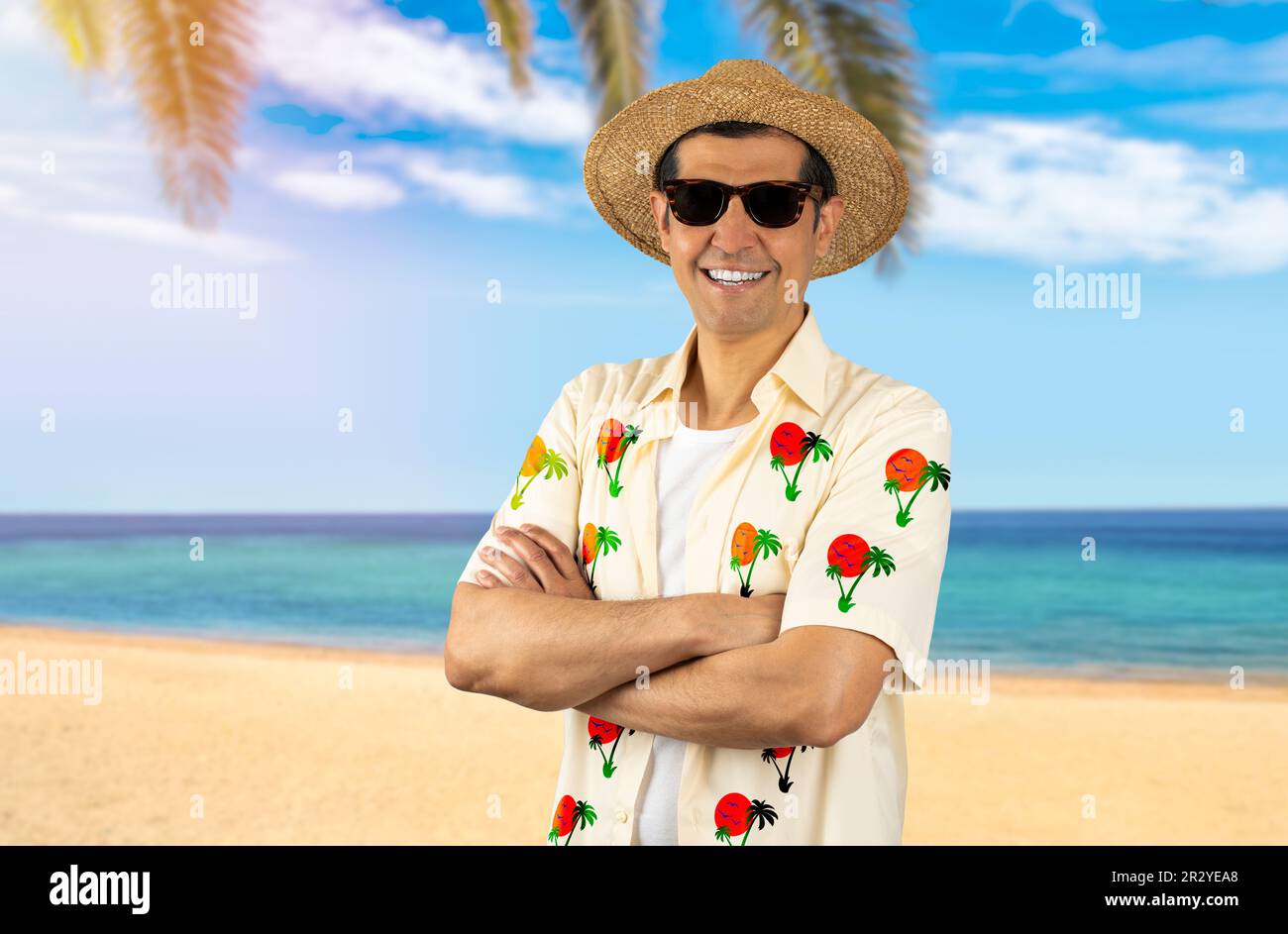 Ein lateinischer Mann im Urlaub, der ein geblümtes Hemd trägt, eine Sonnenbrille am Strand trägt, ein fröhliches Gesicht, das mit gekreuzten Armen lächelt und in die Kamera schaut. Positive Person. Stockfoto