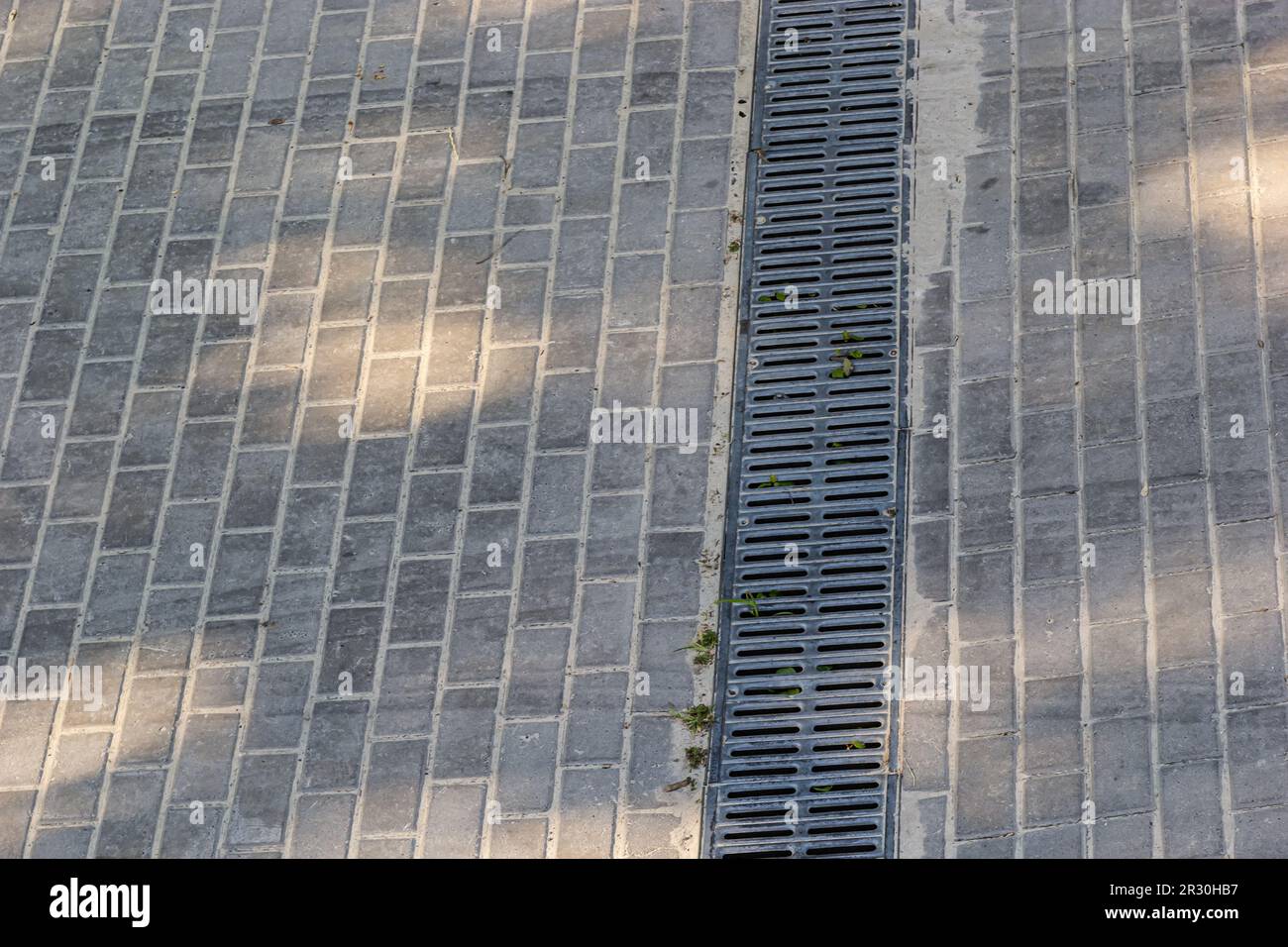 Ein Gitter eines Drainage-Pflastersystems auf einem Fußweg aus quadratischen Steinfliesen, Nahaufnahme eines Regenwasser-Entwässerungssystems. Stockfoto