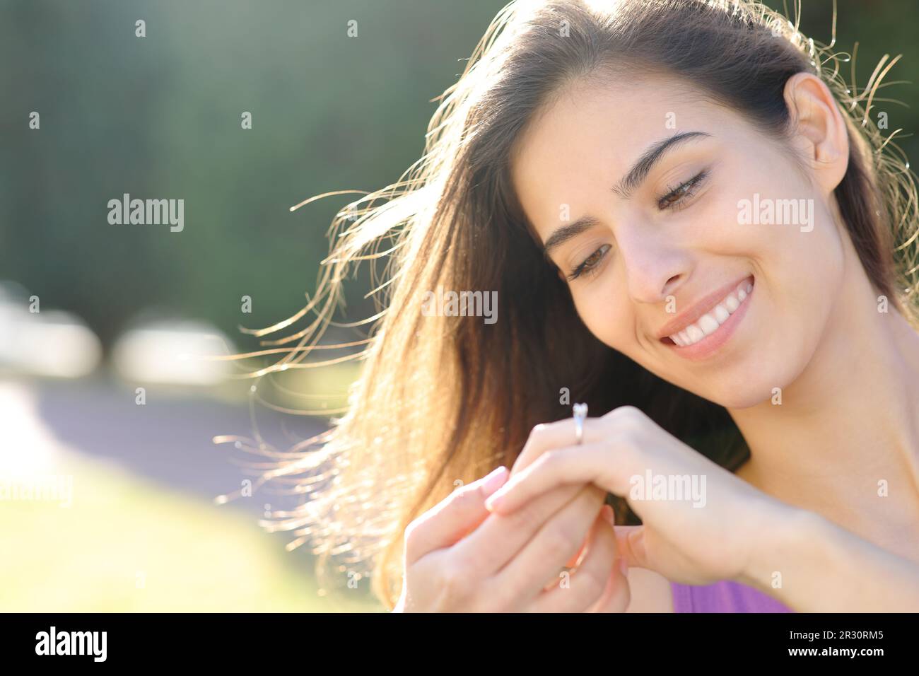 Glückliche Verlobte, die auf einen Verlobungsring schaut, der in einem Park sitzt Stockfoto