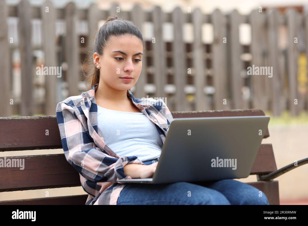 Ein ernster Teenager, der ein Notebook auf einer Bank im Park benutzt Stockfoto