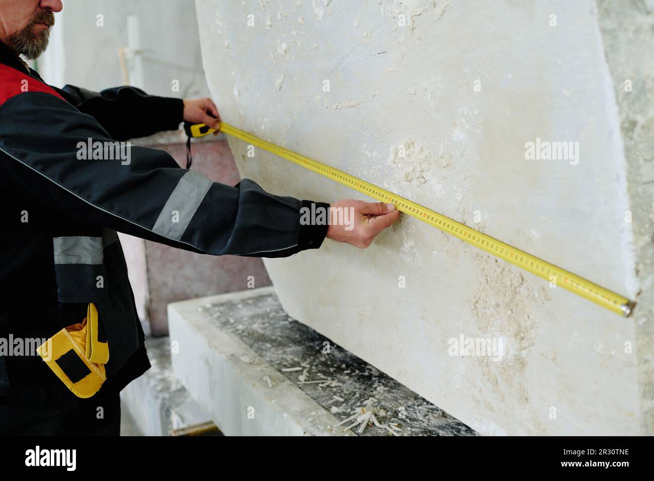 Nahaufnahme des Arbeiters, der das große Stück Stein mit dem Lineal während der Arbeit in der Anlage misst Stockfoto