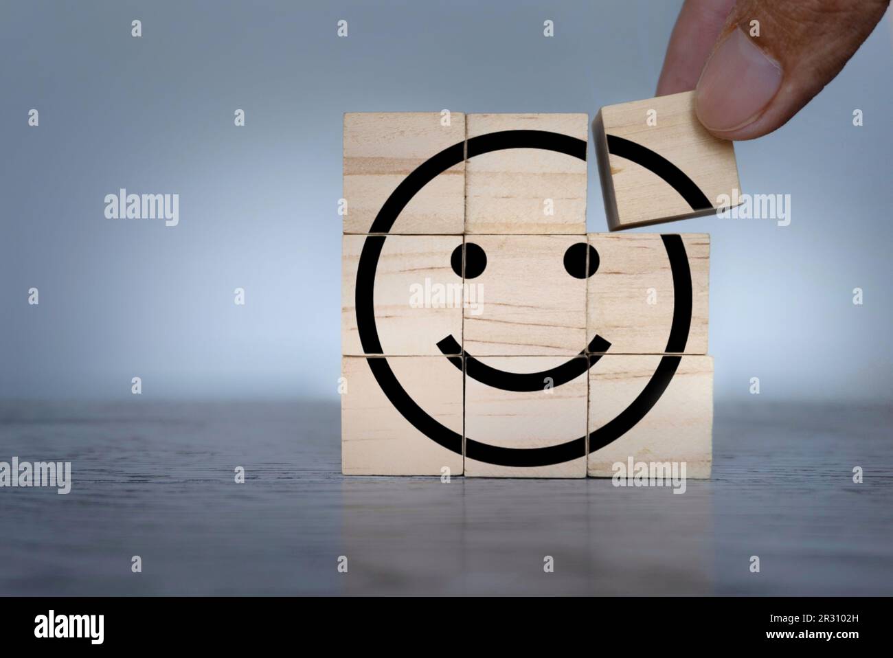 Ein hölzerner Würfel mit einem Smiley-Symbol wird von Hand platziert. Psychische Gesundheit, Wellness und gesunder Geist Stockfoto
