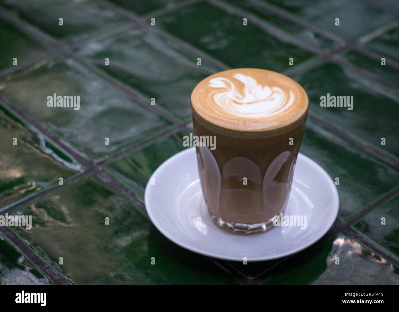 Flacher weißer Kaffee in einer Tasse aus Glas auf einem grün gefliesten Tisch. Speicherplatz kopieren. Stockfoto