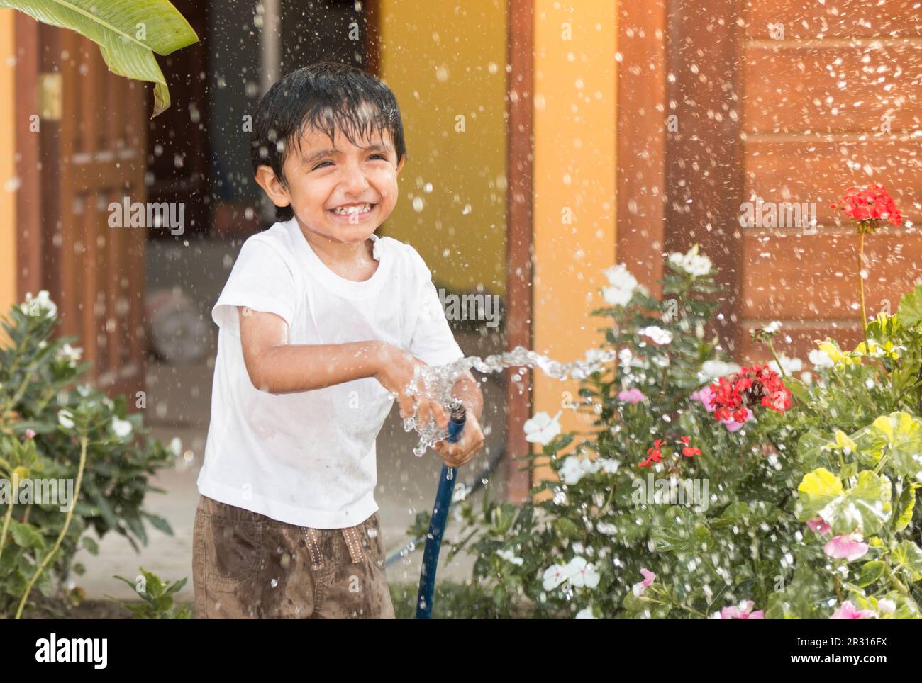 Das Kind spielt mit Wasser, während es den Garten bewässert Stockfoto