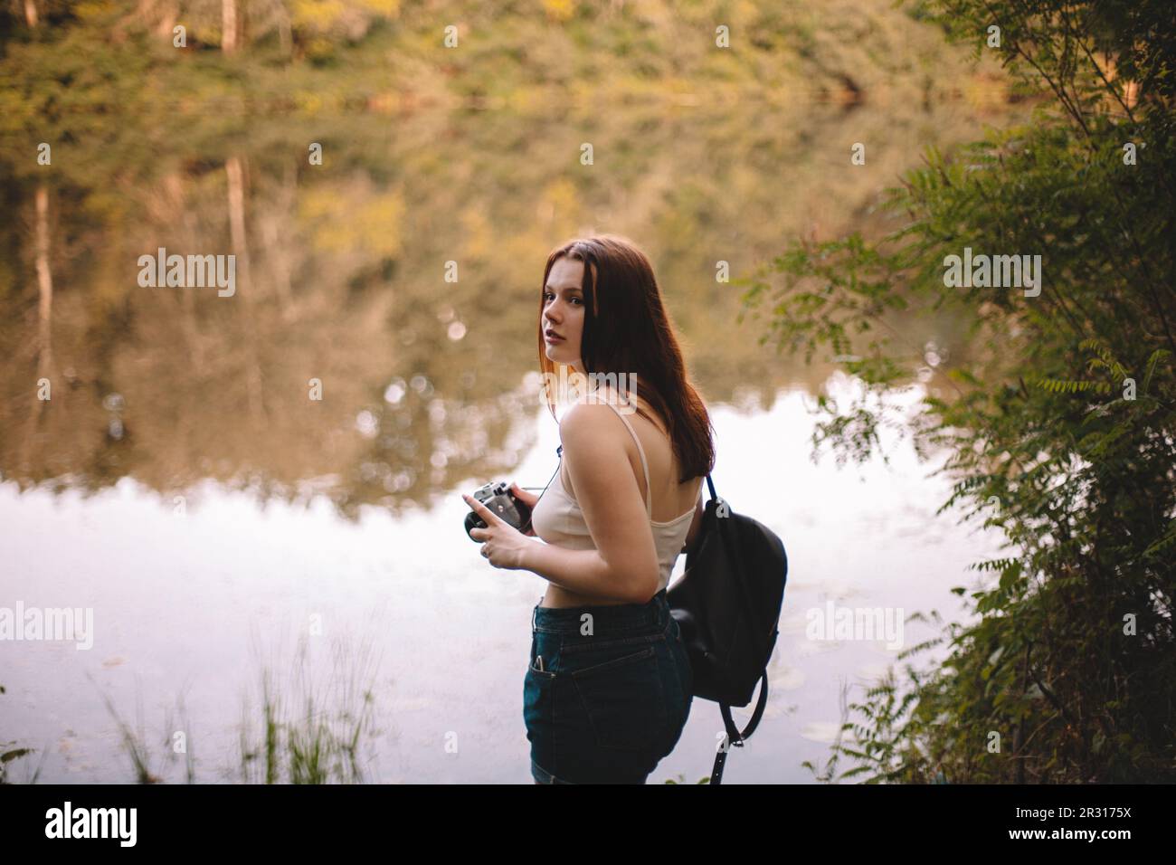 Weibliche Reisende mit Kamera am See im Wald Stockfoto