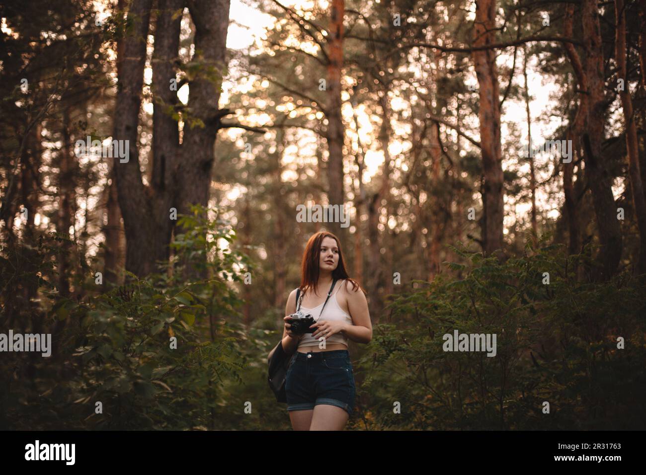 Eine junge Frau, die eine Kamera hält, während sie im Wald läuft Stockfoto
