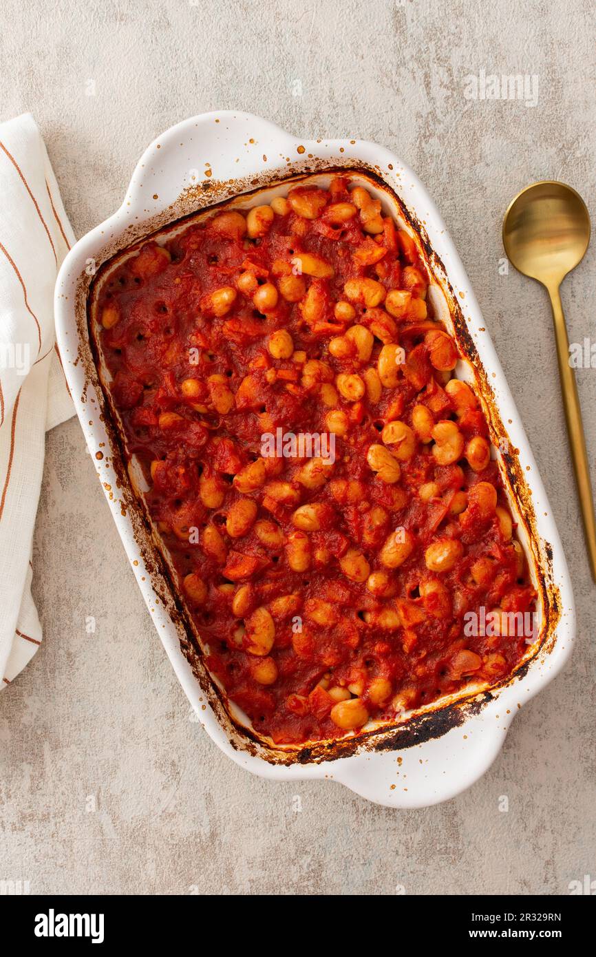 Gesundes Frühstück und Mittagessen, gedünstete weiße Bohnen mit Karotten, Zwiebeln und Tomaten, Blick von oben auf eine ovale Keramikrösterei mit gedünsteten Hülsenfrüchten Stockfoto