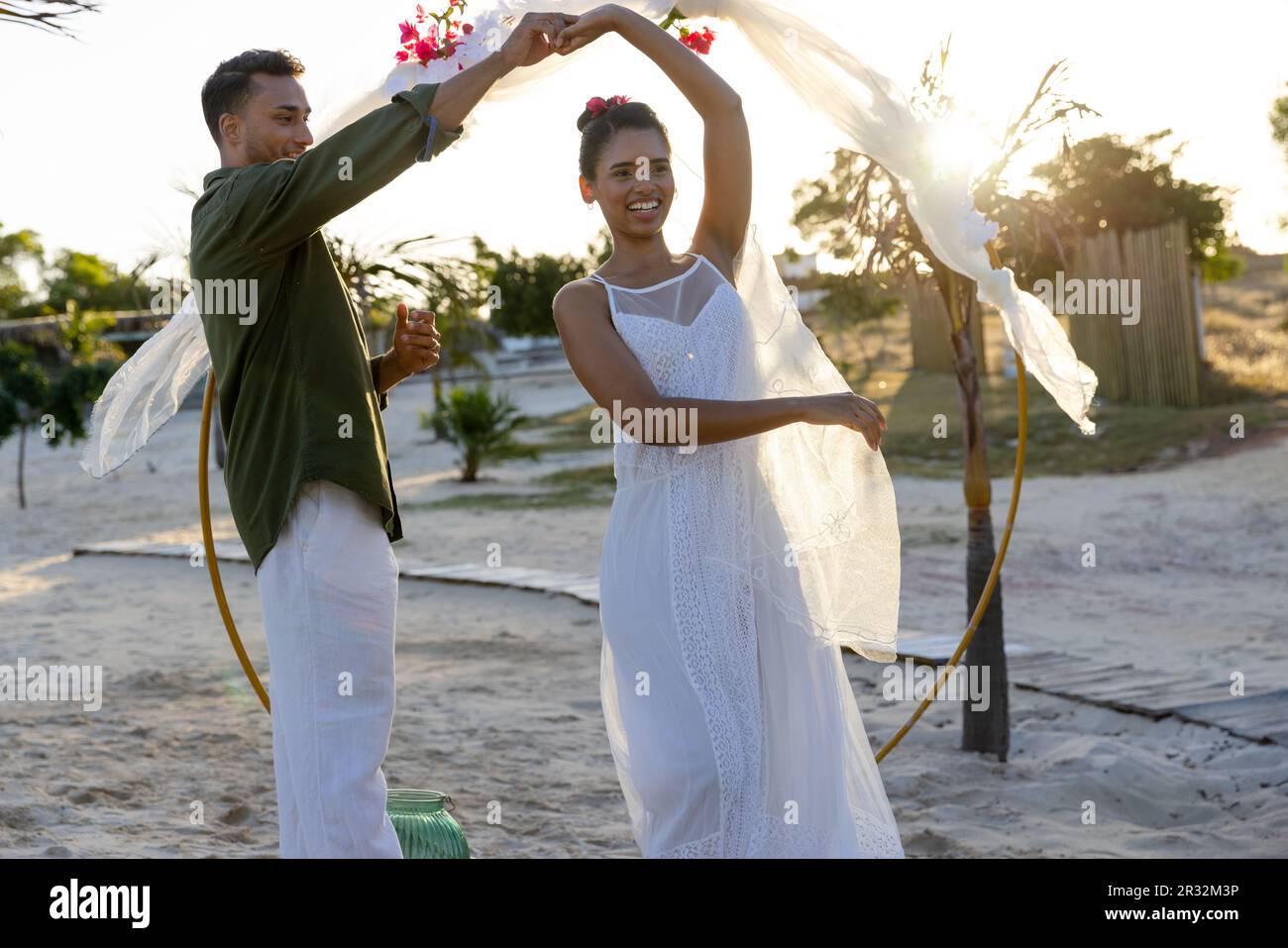 Fröhliche, vielfältige Braut und Bräutigam tanzen auf ihrer Hochzeit am Strand Stockfoto