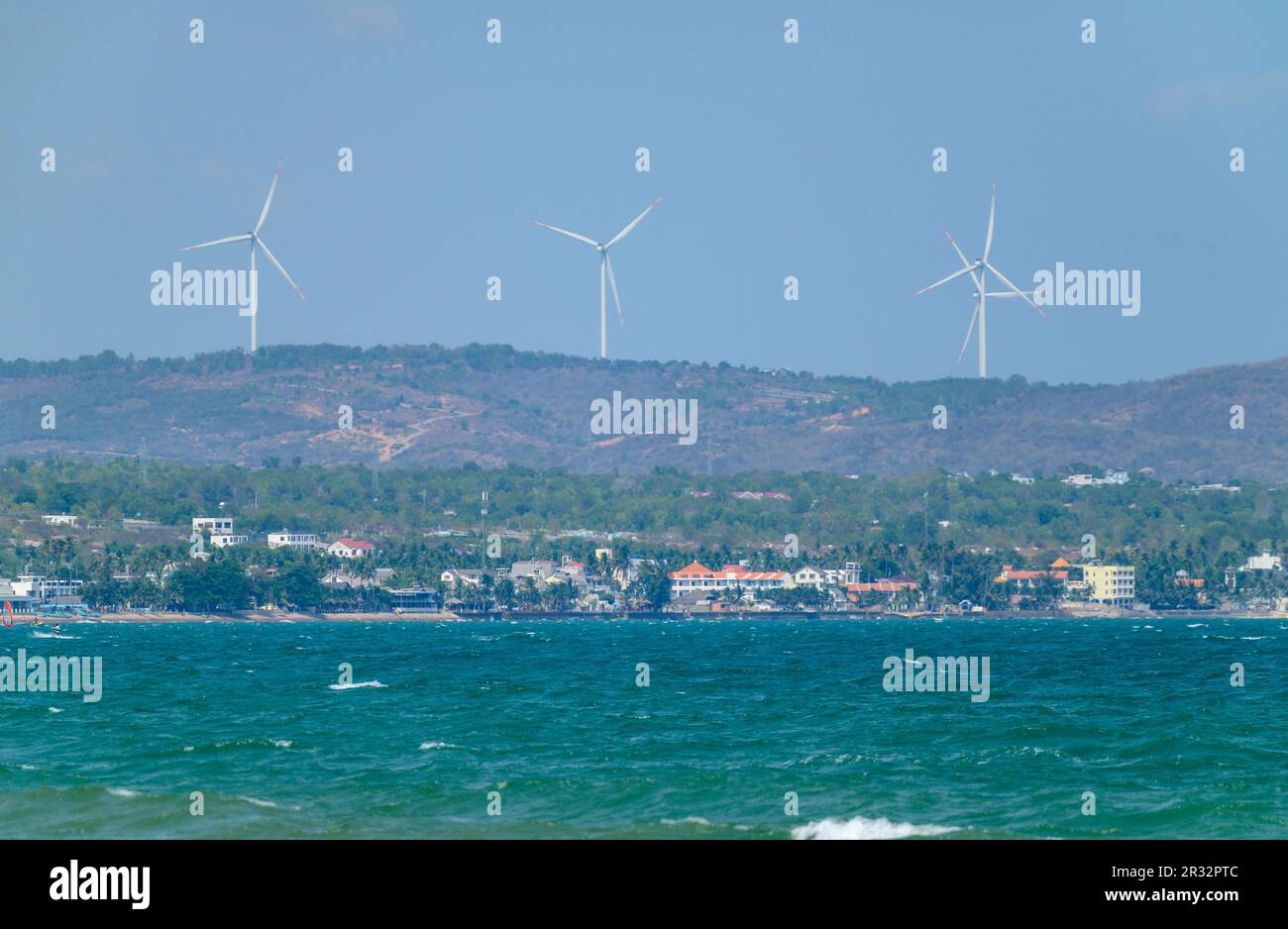 Ein Blick über die Bucht in Mui Ne in Richtung des langen Strandes und Windkraftturbinen auf dem Hügel, Vietnam. Stockfoto