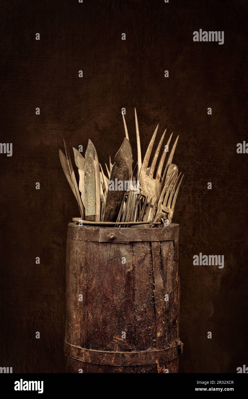 Antiker Holzfass mit Gabeln, Messern und Löffeln vor einem verwitterten braunen Hintergrund Stockfoto