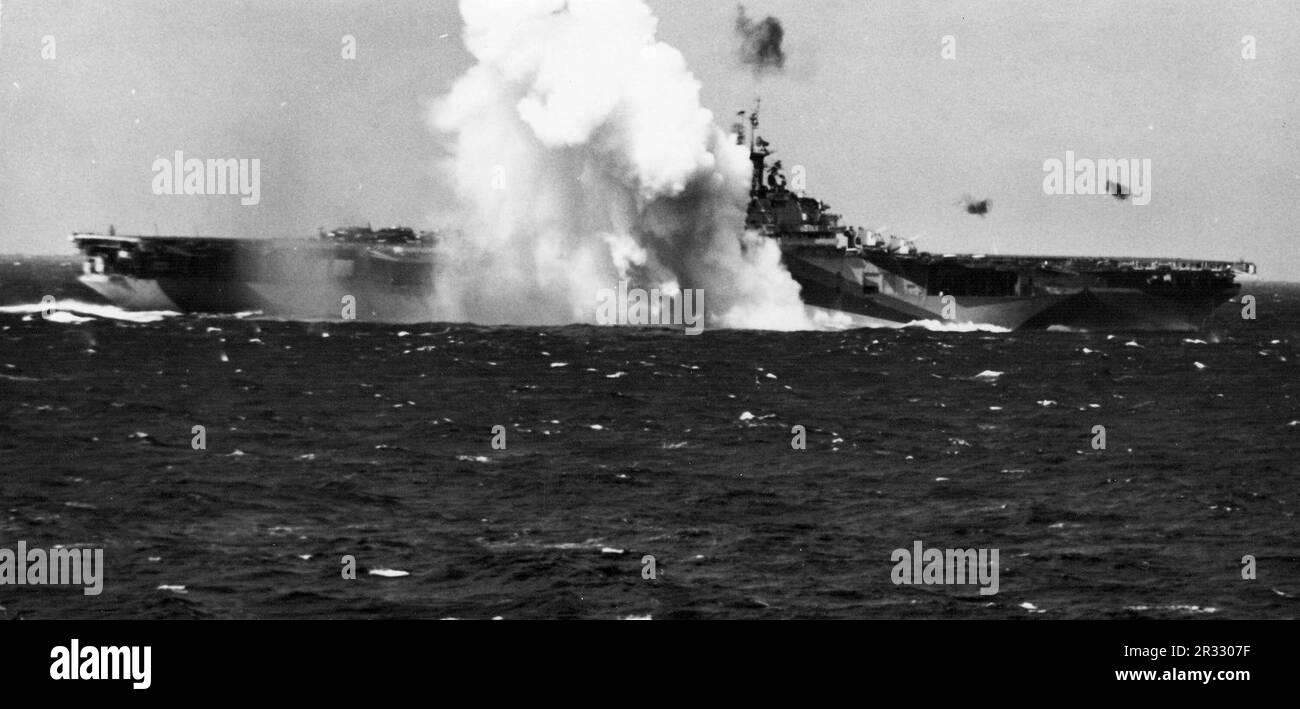Ein Kamikaze-Selbstmordflugzeug spritzt in der Nähe der USA Navy-Flugzeugträger USS Ticonderoga (CV-14) auf dem Weg vor den Philippinen. Als Japan Ende 1944 mit einer Niederlage konfrontiert war, entschied es sich, US-Schiffe mit Selbstmordattentaten, bekannt als Kamikaze, zu zerstören. Diese Angriffe waren eine starke physische und psychologische Waffe und versenkten insgesamt 47 Schiffe zu einem Preis von mehr als 3000 Piloten und Flugzeugen. Ende 1944 war die US-Marine so groß, dass die Verluste unbedeutend waren und den Verlauf des Krieges nicht veränderten. Stockfoto