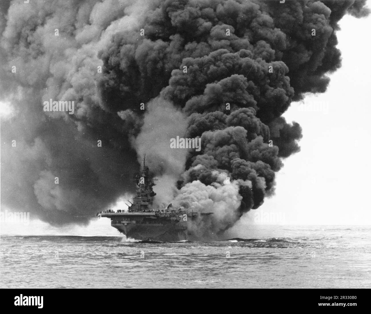 Die USA Navy Aircraft Carrier USS Bunker Hill (CV-17) brennt nach dem Zusammenstoß von zwei „Kamikaze“-Selbstmordflugzeugen vor Okinawa am 11. Mai 1945. Fotografiert von USS Bataan (CVL-29). Der Streik fing voll betankte und bewaffnete Flugzeuge an Deck und löste sehr gefährliche Brände aus. Obwohl das Schiff schwer beschädigt war, ging es nicht unter und kehrte zur Reparatur in die USA zurück. Das Schiff wurde 1966 stillgelegt und 1973 verschrottet. Stockfoto Die USA Navy Aircraft Carrier USS Bunker Hill (CV-17) brennt nach dem Zusammenstoß von zwei „Kamikaze“-Selbstmordflugzeugen vor Okinawa am 11. Mai 1945. Fotografiert von USS Bataan (CVL-29). Der Streik fing voll betankte und bewaffnete Flugzeuge an Deck und löste sehr gefährliche Brände aus. Obwohl das Schiff schwer beschädigt war, ging es nicht unter und kehrte zur Reparatur in die USA zurück. Das Schiff wurde 1966 stillgelegt und 1973 verschrottet. Stockfoto