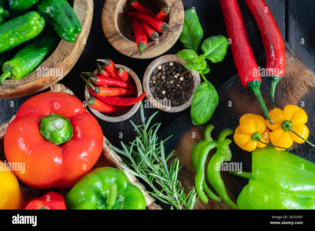 Eine farbenfrohe Auswahl an Paprika, heißem Paprika und Chili, dekoriert mit verschiedenen Assesoires auf einem Holztisch. Stockfoto