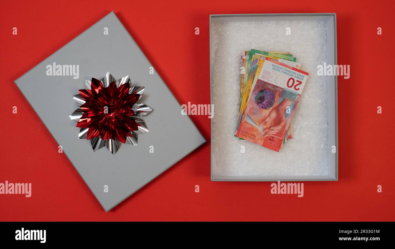 Möglichkeit, Geld zu spenden (schweizer Franken CHF) als Geschenk. Geld als Geschenk zu geben. Ein Geldgeschenk in einer silbernen, modernen Kiste, eine rote silberne Schleife, falscher Schnee Stockfoto