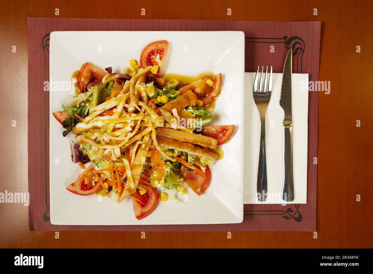 Ein Salat mit panierten gebratenen Hähnchenstreifen, Tomatenstückchen, Salat, Zuckermais und süßer Senf Vinaigrette Stockfoto
