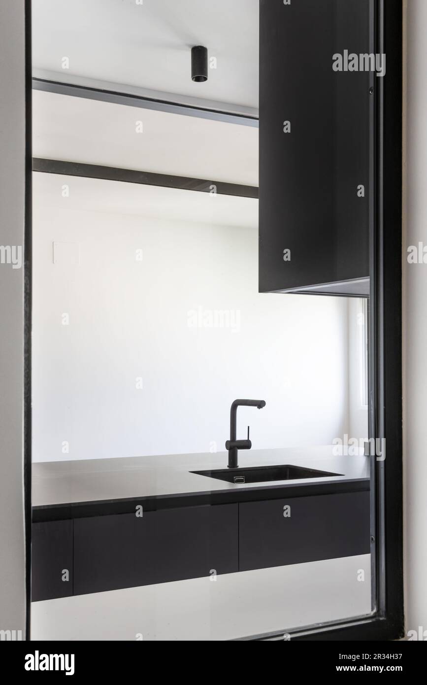Ein Oberlicht in einer Küche, ausgestattet mit glatten schwarzen Schränken ohne Griffe, einem schwarzen Waschbecken mit passendem Wasserhahn und schwarzer Schienenbeleuchtung Stockfoto