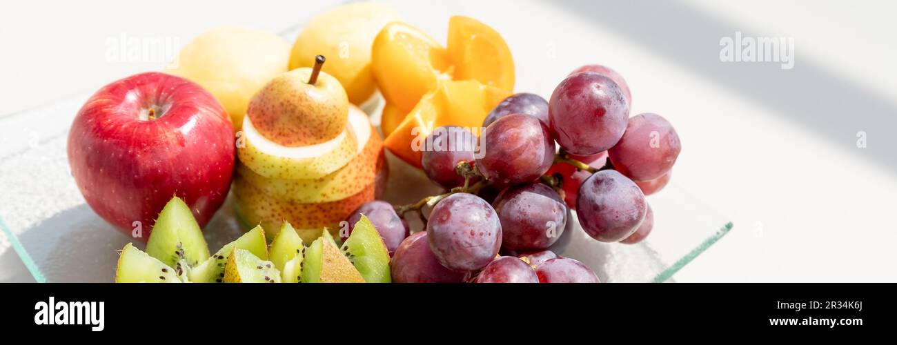 Rohe Früchte Beeren Platter, Mango, Orangen, Kiwi, Erdbeeren, Blaubeeren grapefruit Trauben, Bananen, Äpfel auf dem weißen Teller, auf dem Weg von weißen Tabl Stockfoto