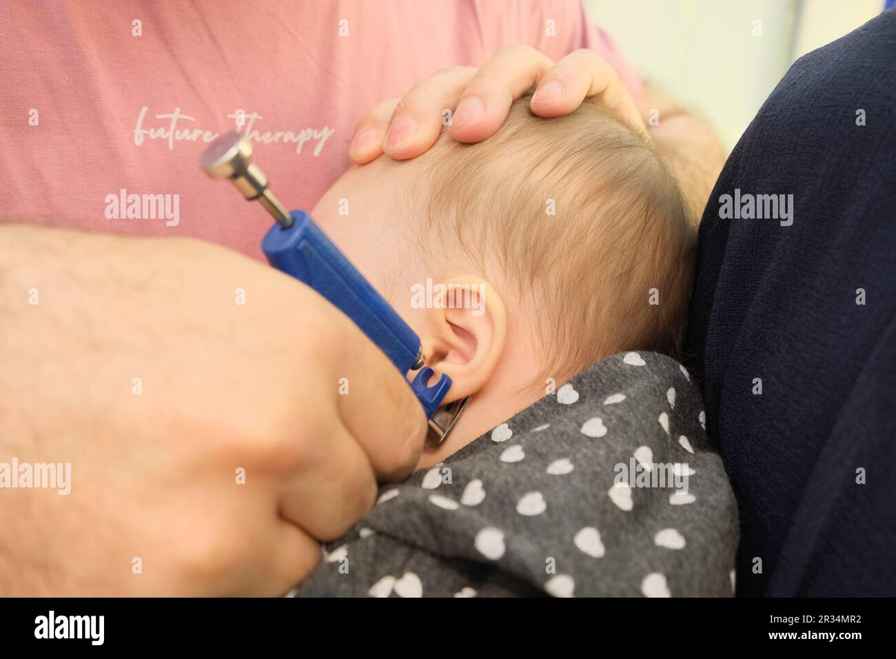 Ein kleines Mädchen, das mit einer speziellen Piercingpistole im Juweliergeschäft Ohrenpiercing macht. Stockfoto