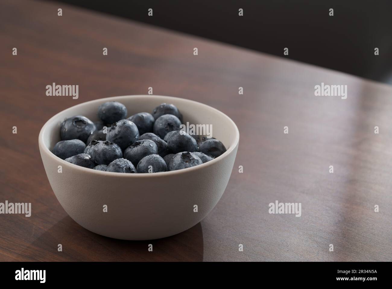 Frisch gewaschene Heidelbeeren in weißer Schüssel auf Walnusstisch, flacher Fokus Stockfoto