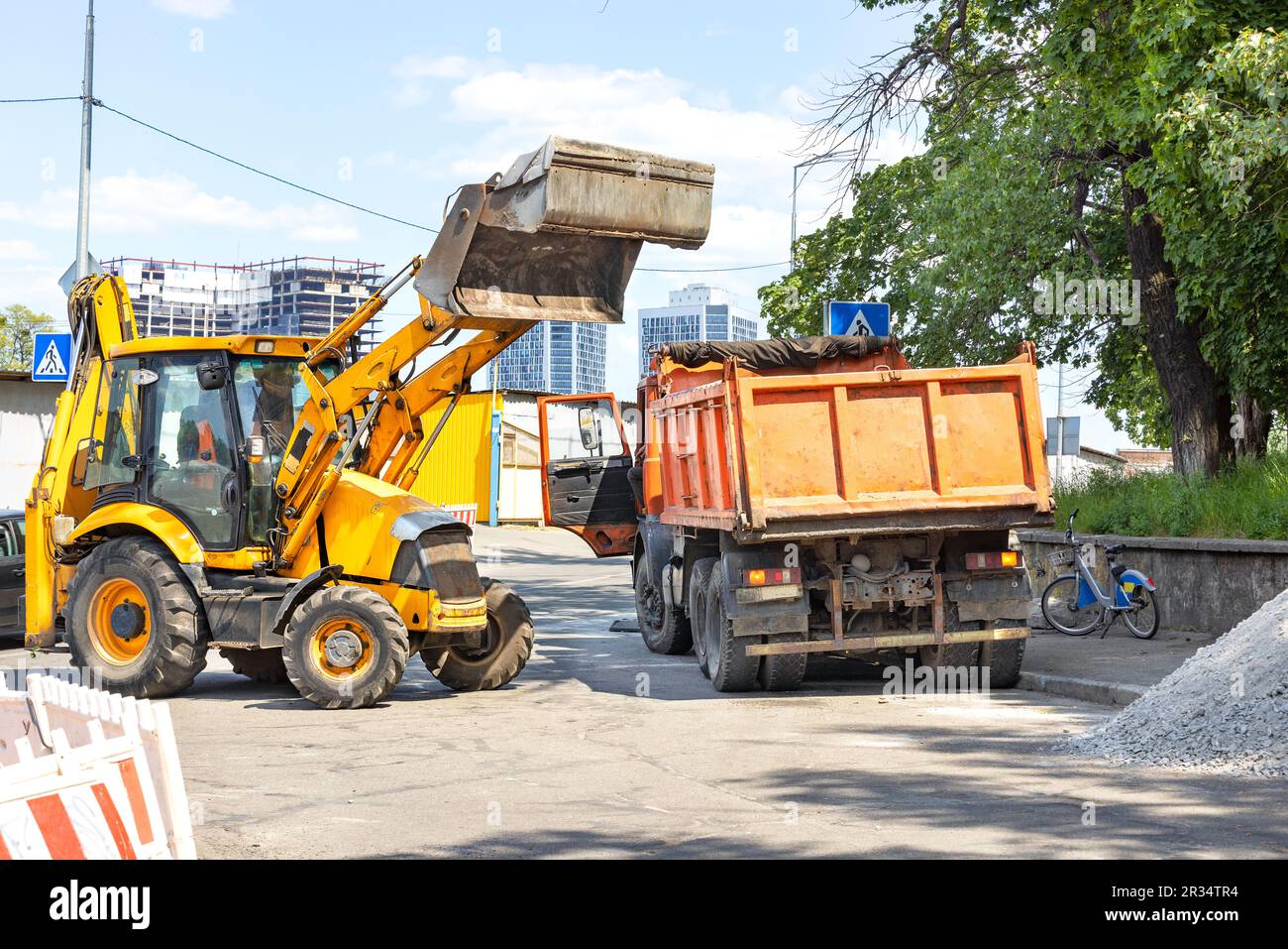 Straßenbaumaschinen, ein Traktor mit hydraulischem Löffel und ein alter Lkw an einem sonnigen Tag an einer Gabelung in einer Stadtstraße. Stockfoto