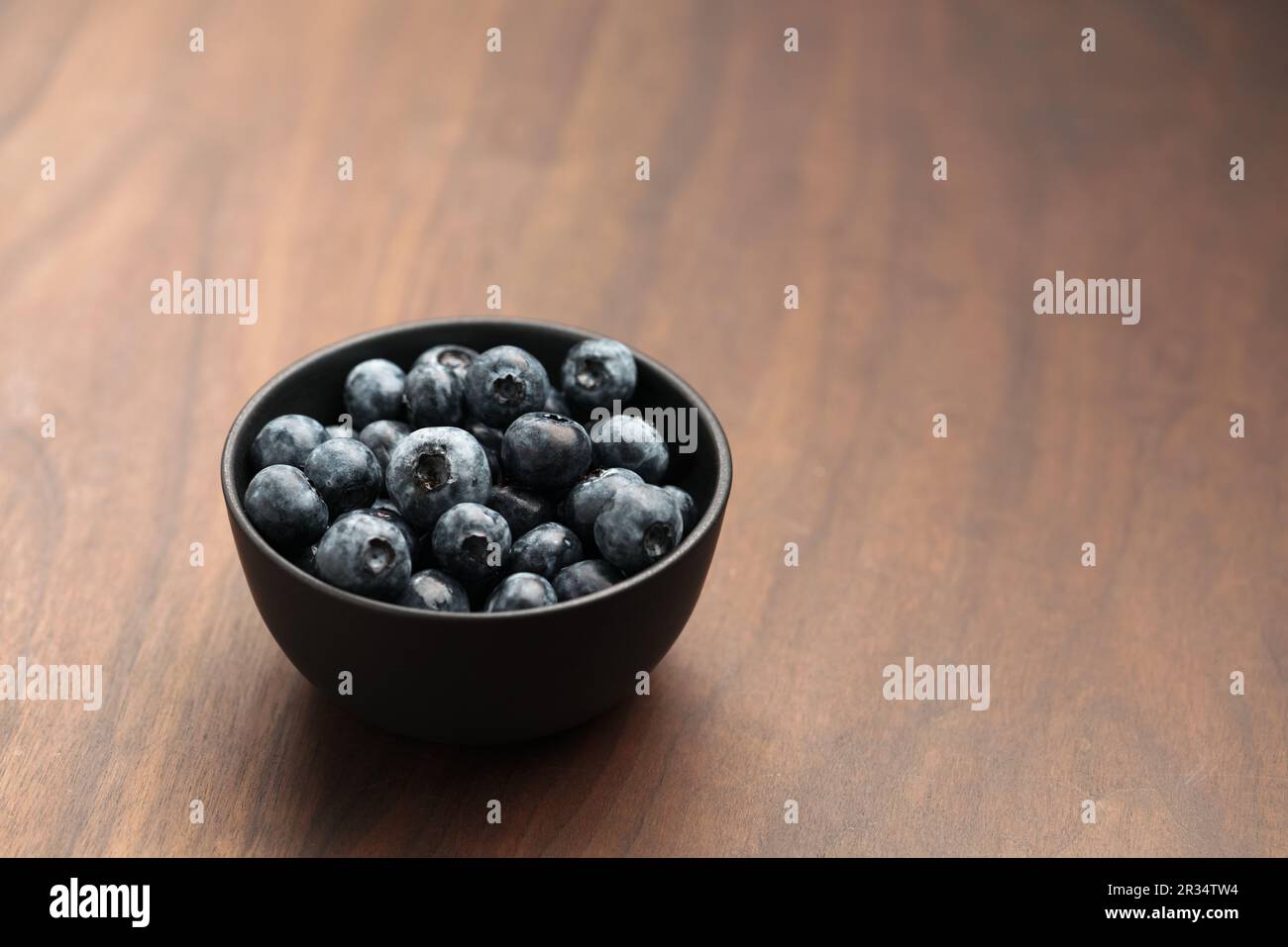 Große Bio-Heidelbeeren in einer schwarzen Schüssel auf Walnusstisch, flacher Fokus Stockfoto