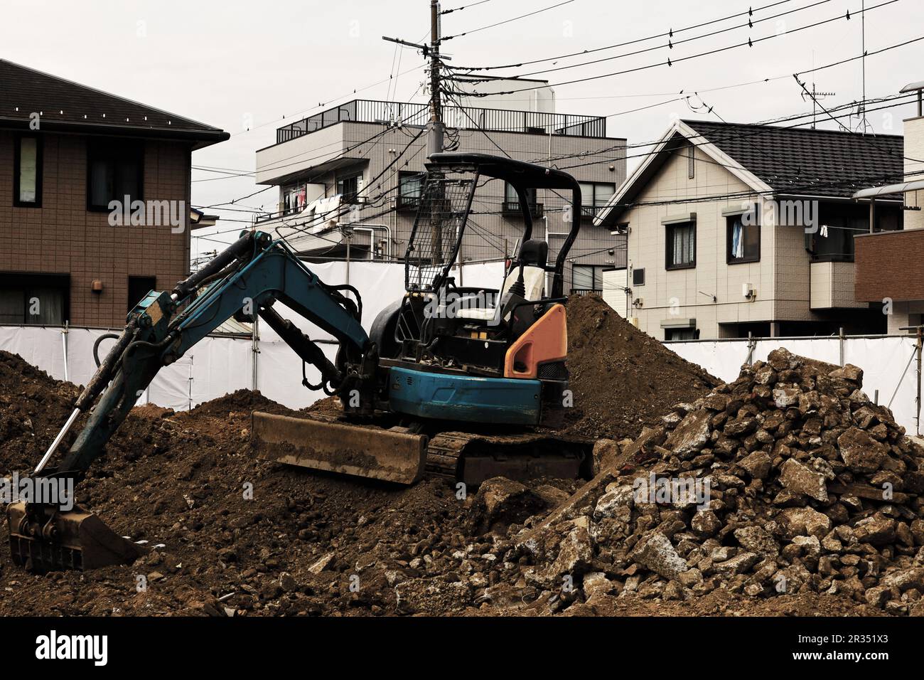 Baustelle in einem Wohngebiet, auf dem ein kleiner Bagger zum Nivellieren des Bodens verwendet wird Stockfoto