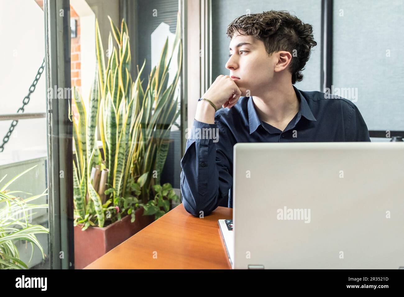 Ein junger, aufmerksamer Mann im Büro, der durchs Fenster schaut. Stockfoto