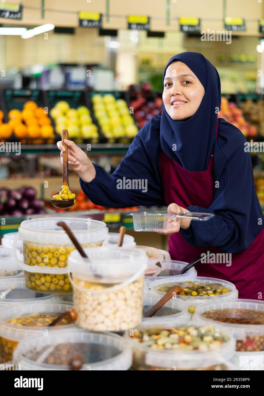 Asiatische Verkäuferin von Hijab legt sorgfältig große eingelegte Oliven in eine Einweg-Lunchbox Stockfoto