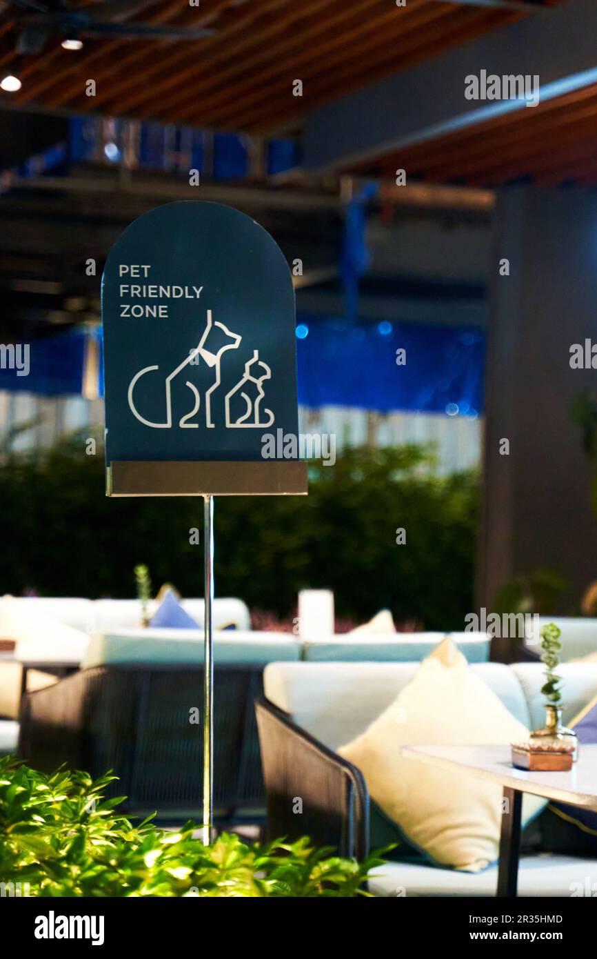 Ein haustierfreundliches Café-Schild auf einer sonnigen Sommerterrasse lädt Haustierbesitzer ein, sich zu entspannen und eine Mahlzeit mit ihren pelzigen Freunden zu genießen. Die warme, einladende Atmosphäre Stockfoto