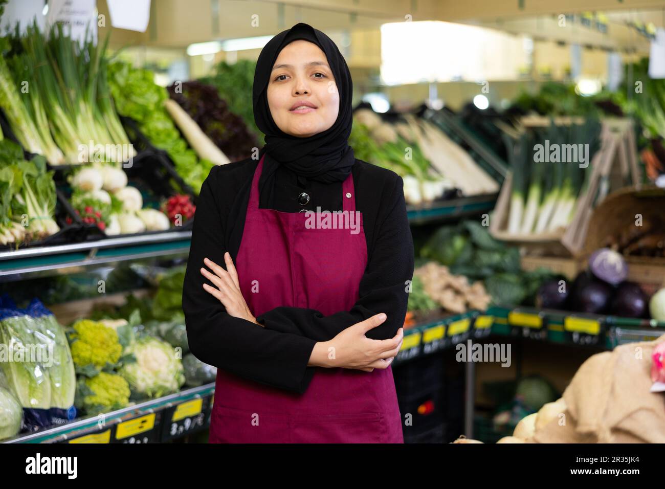 Muslimische Verkäuferin in Hijab steht mit verschränkten Armen auf der Brust und wartet auf Kunden Stockfoto