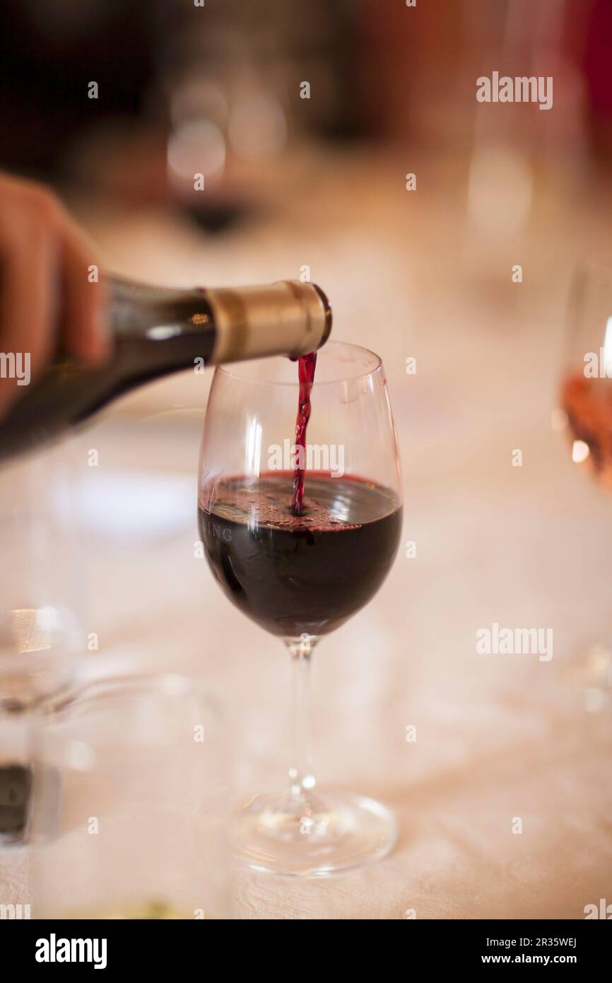 Rotwein wird aus einer Flasche in ein Glas gegossen Stockfoto