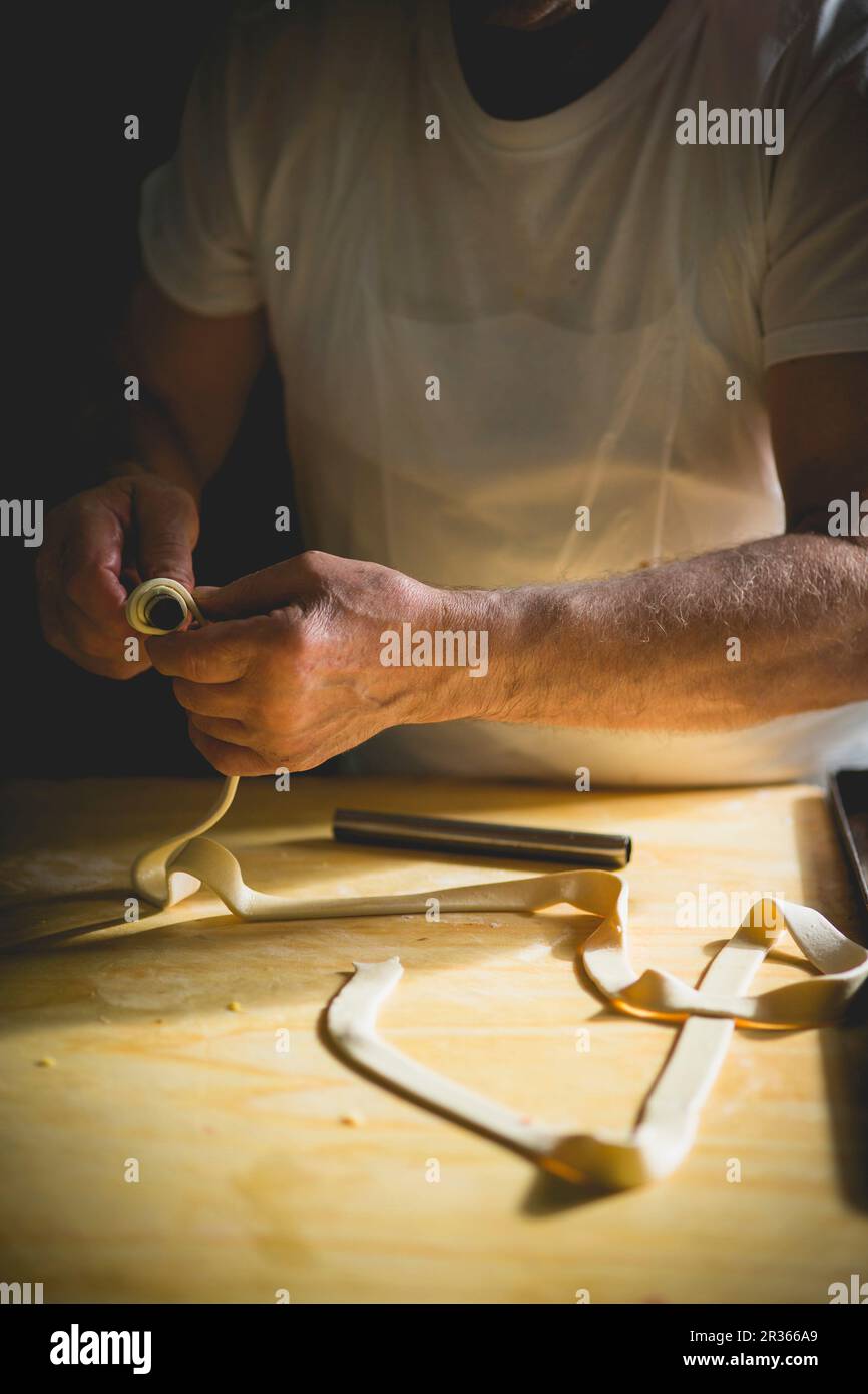 Ein Konditor, der ein Stück Gebäck um einen Metallstab rollt Stockfoto